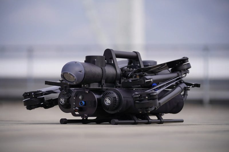 Compact black CADDIS unmanned aircraft with folded components resting on its landing skids.
