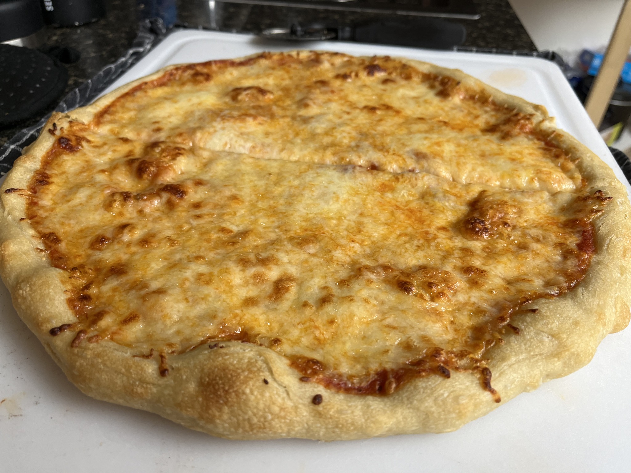 A round cheese pizza with a golden surface and large browned bubbles on a white cutting board.