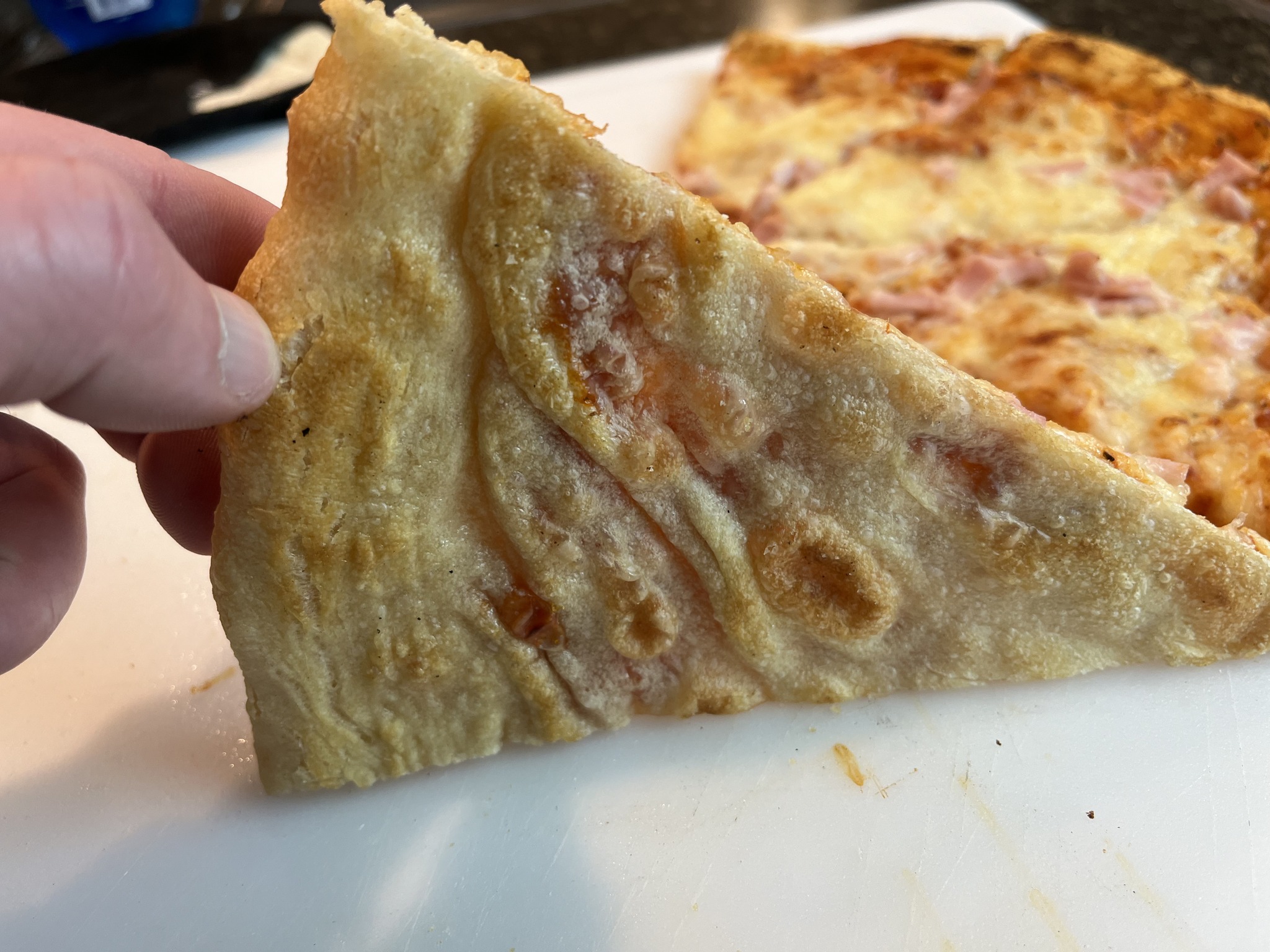 The underside of a pizza slice held above the cutting board.