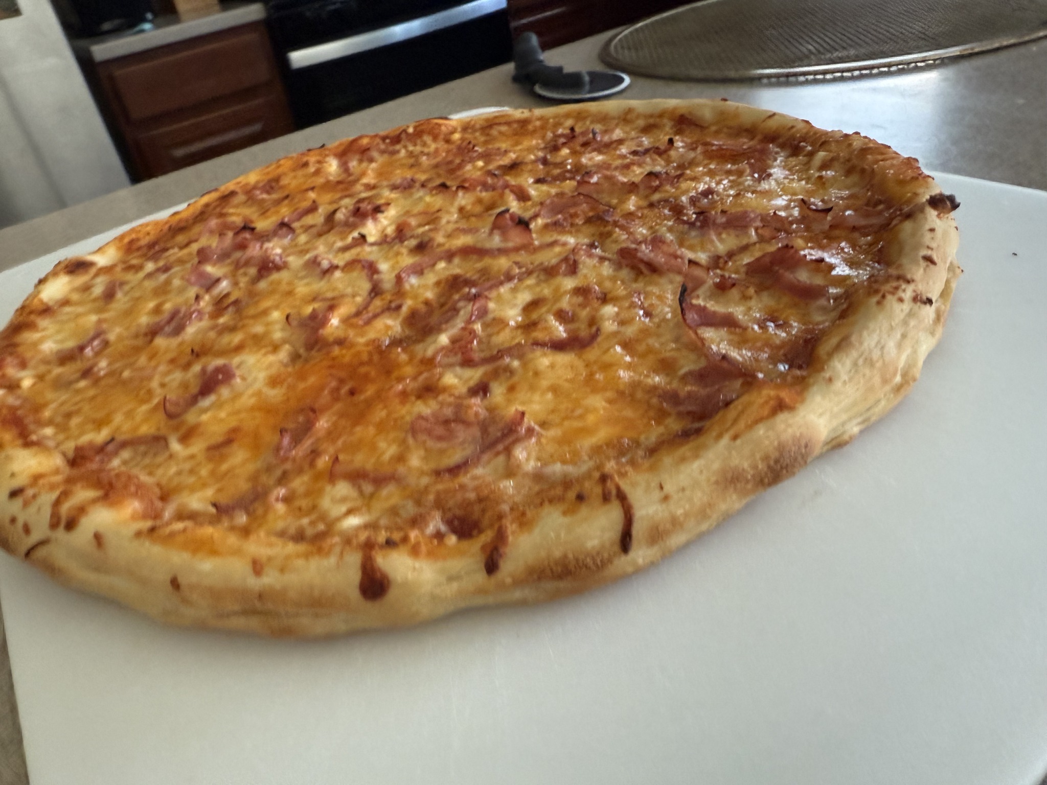 A homemade pizza with browned cheese, thin pink ham-like strips and a broad golden rim on a white cutting board.
