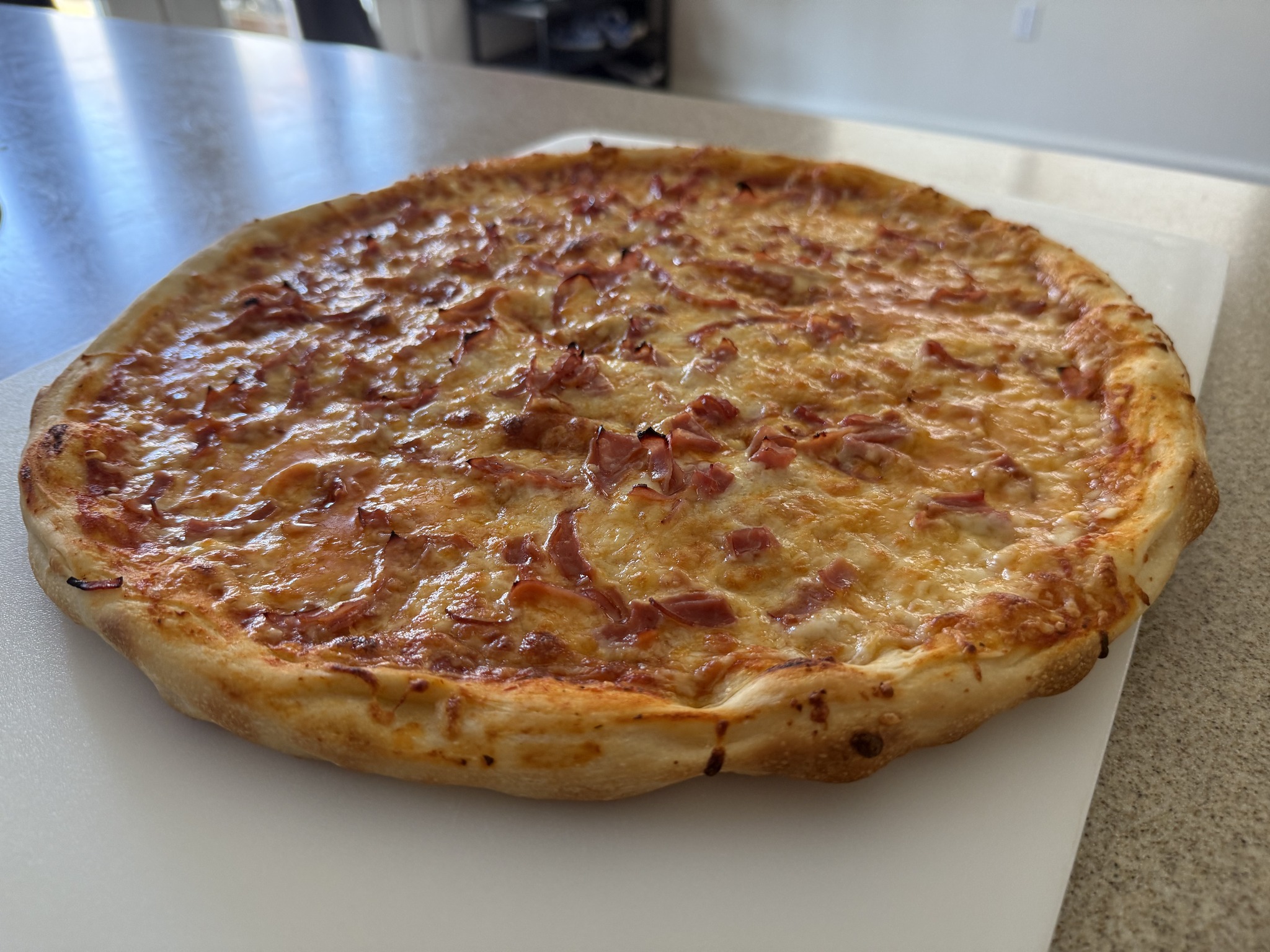 A more overhead view of the same homemade pizza, showing the distribution of thin pink topping strips across the cheese.