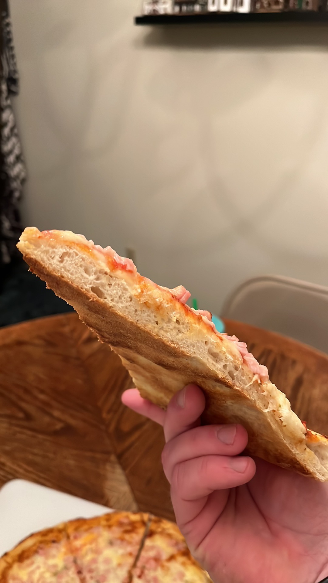 A slice held sideways to show the open pockets inside its crust and the thin base under the toppings.