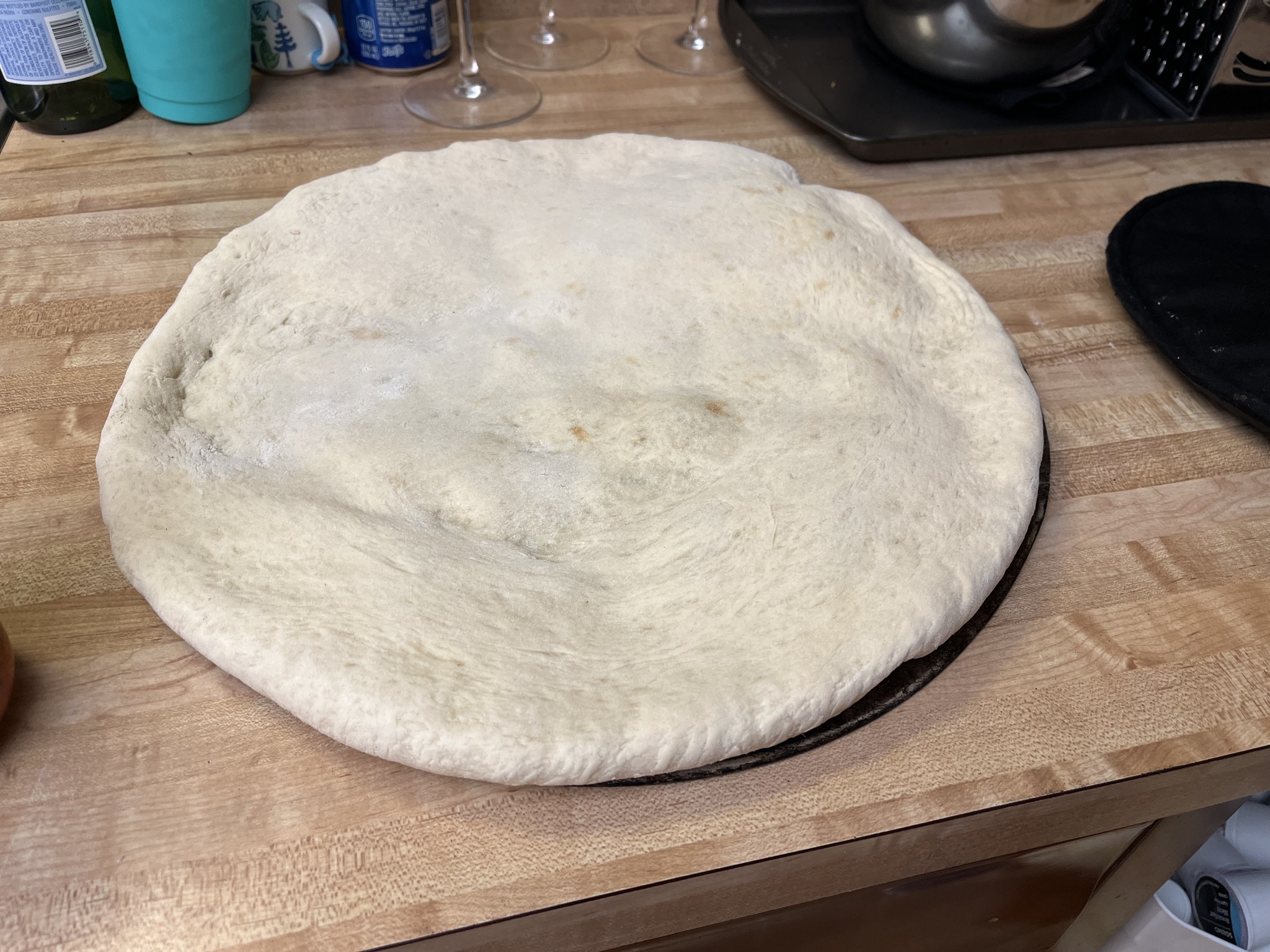 An untopped pizza base resting on a round pizza screen on the kitchen counter.