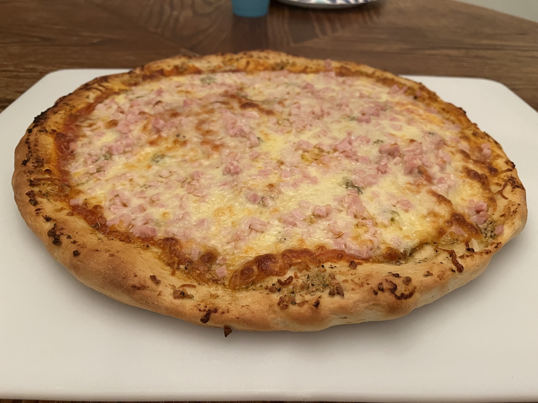 A homemade pizza with browned cheese, a pink diced topping and a broad seasoned-looking rim on a white cutting board.