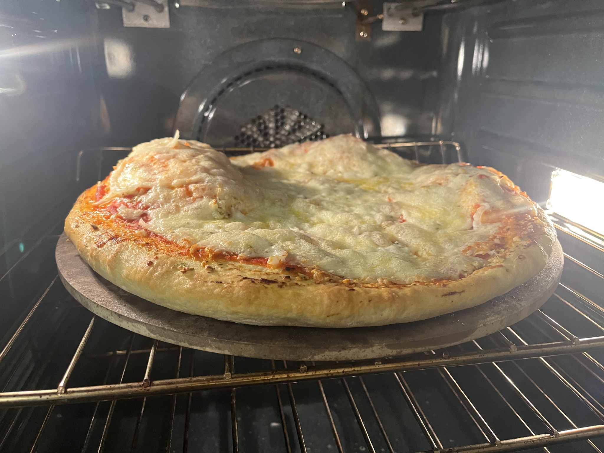 The onion pizza inside the kitchen oven with melted cheese over large raised bubbles.