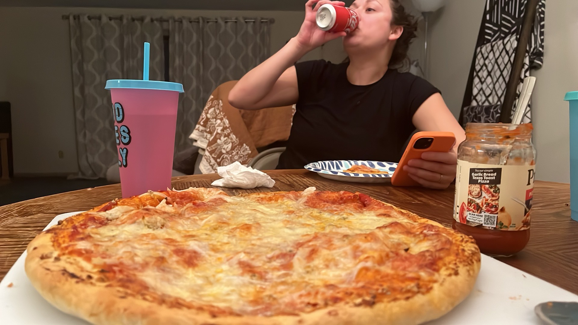 A finished cheese pizza on a white board at the dining table with a person eating behind it.