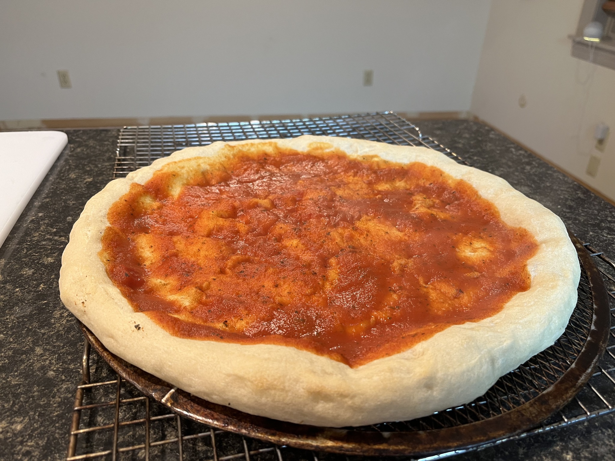 A pizza base covered with red sauce on a round pizza screen.