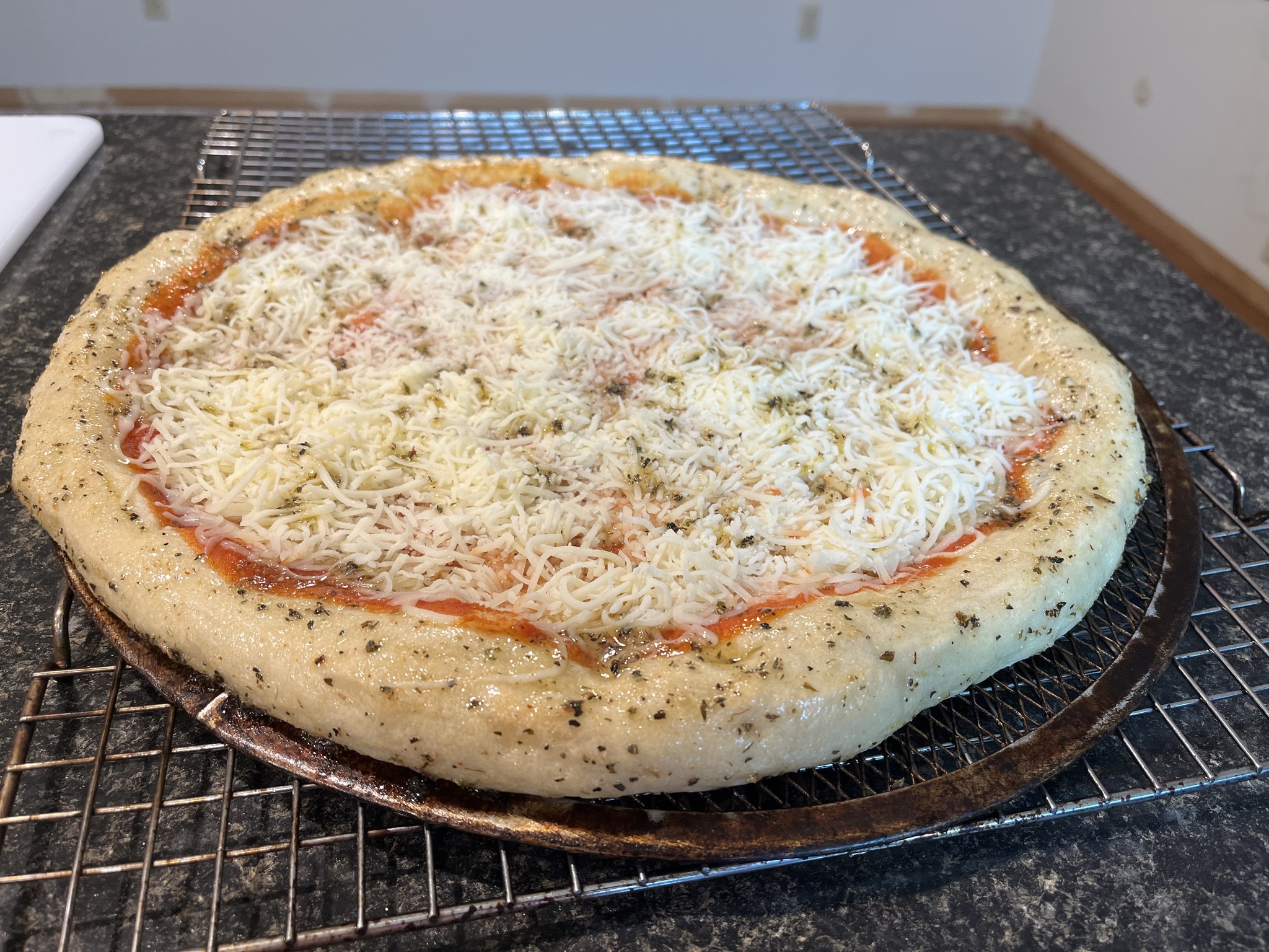 The assembled cheese pizza with a glossy herb-speckled coating around its rim.