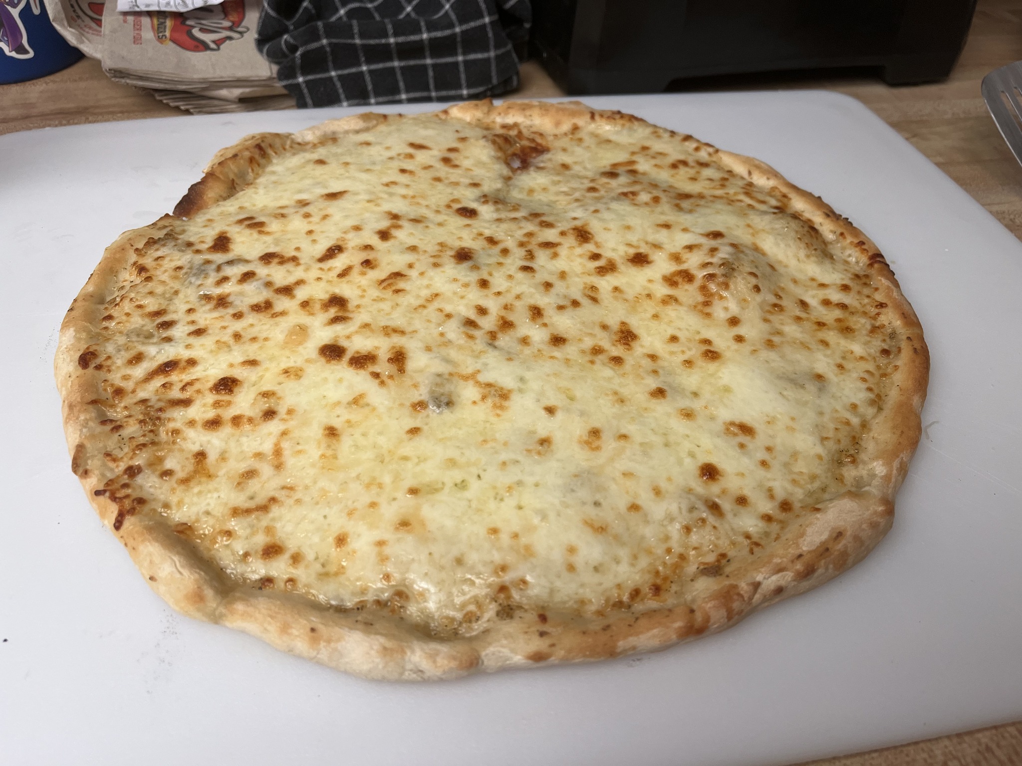 A round homemade cheese pizza with a pale raised rim and lightly golden cheese on a white cutting board.