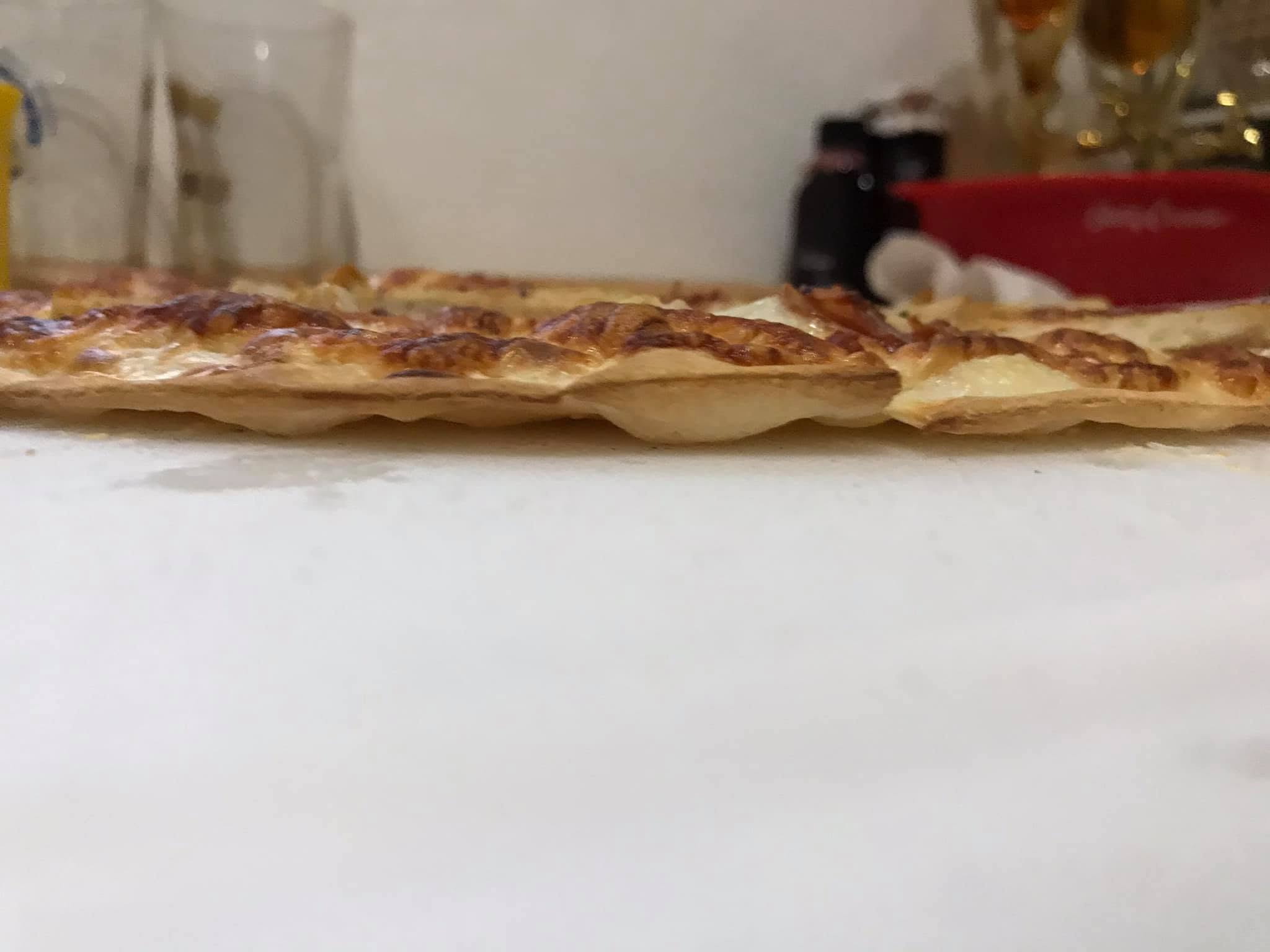 Side view of the baked flammkuchen showing its thin crust and browned topping.