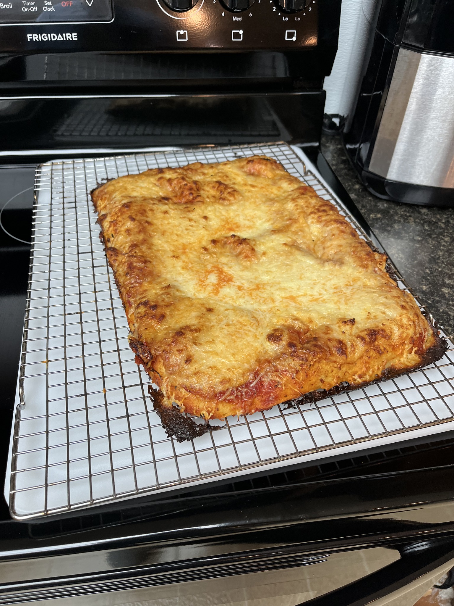 An overhead view of the rectangular pizza on its cooling rack over the stove.