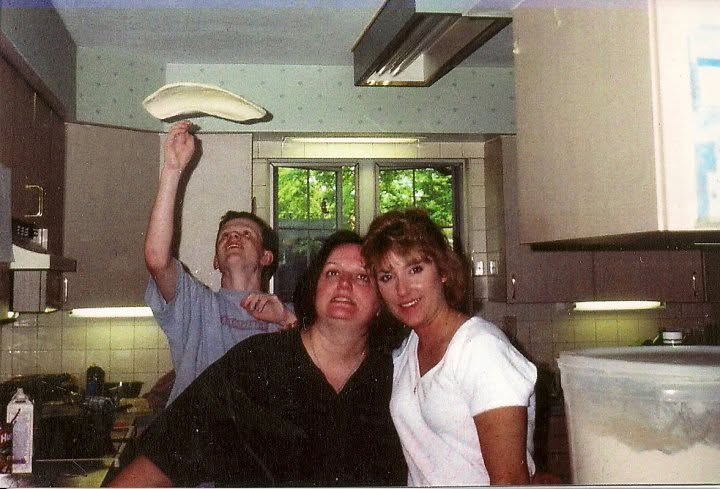 An older family kitchen photograph with pizza dough in midair above an outstretched hand and two people in the foreground.