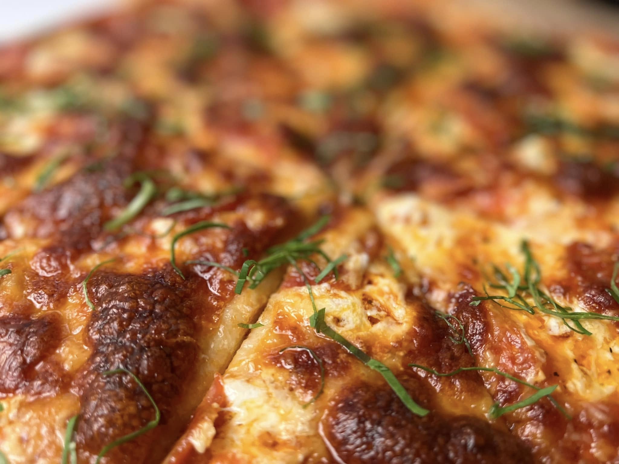 Close-up of a pepperoni pizza with browned cheese and thin green herb strips.