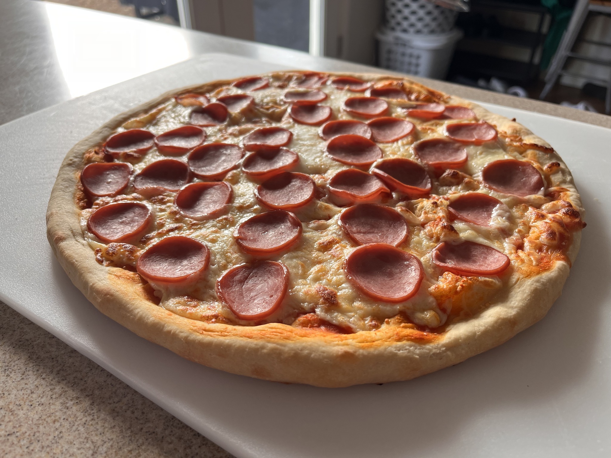 A finished pizza covered with round pink meat slices and melted cheese on a white cutting board.