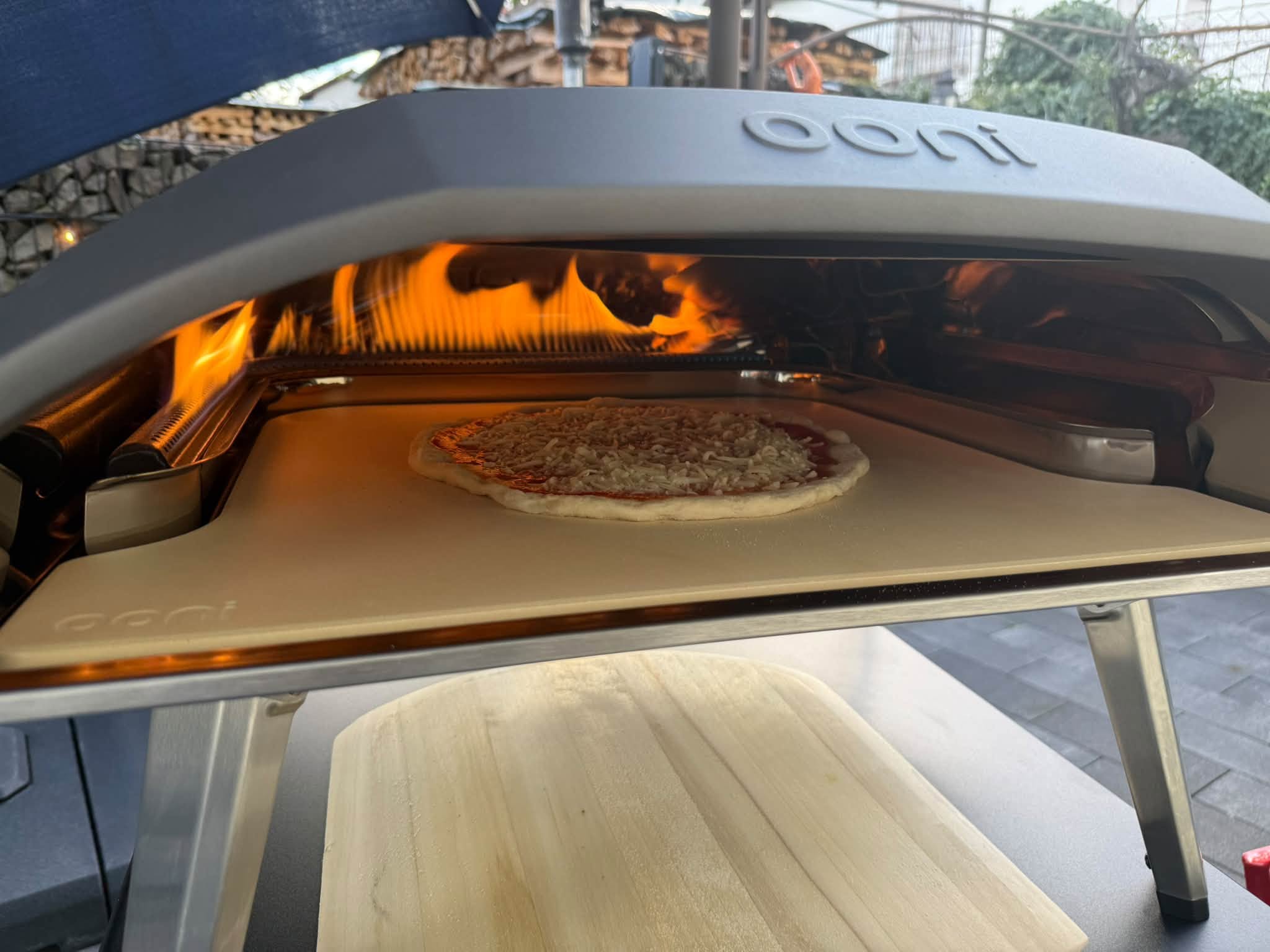 A pizza baking inside an Ooni oven with flames along the back and side.