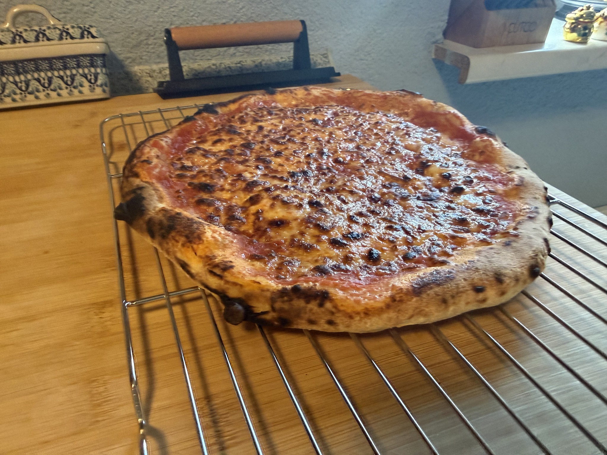A wider view of the finished Ooni pizza, showing the raised, char-spotted rim and browned cheese on a cooling rack.