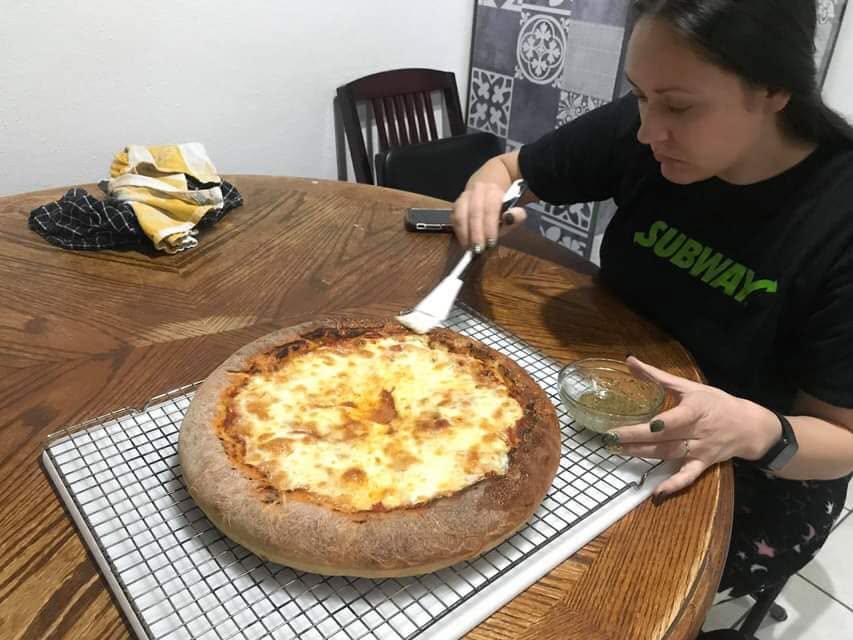 An adult brushing the crust of a pizza at a table.