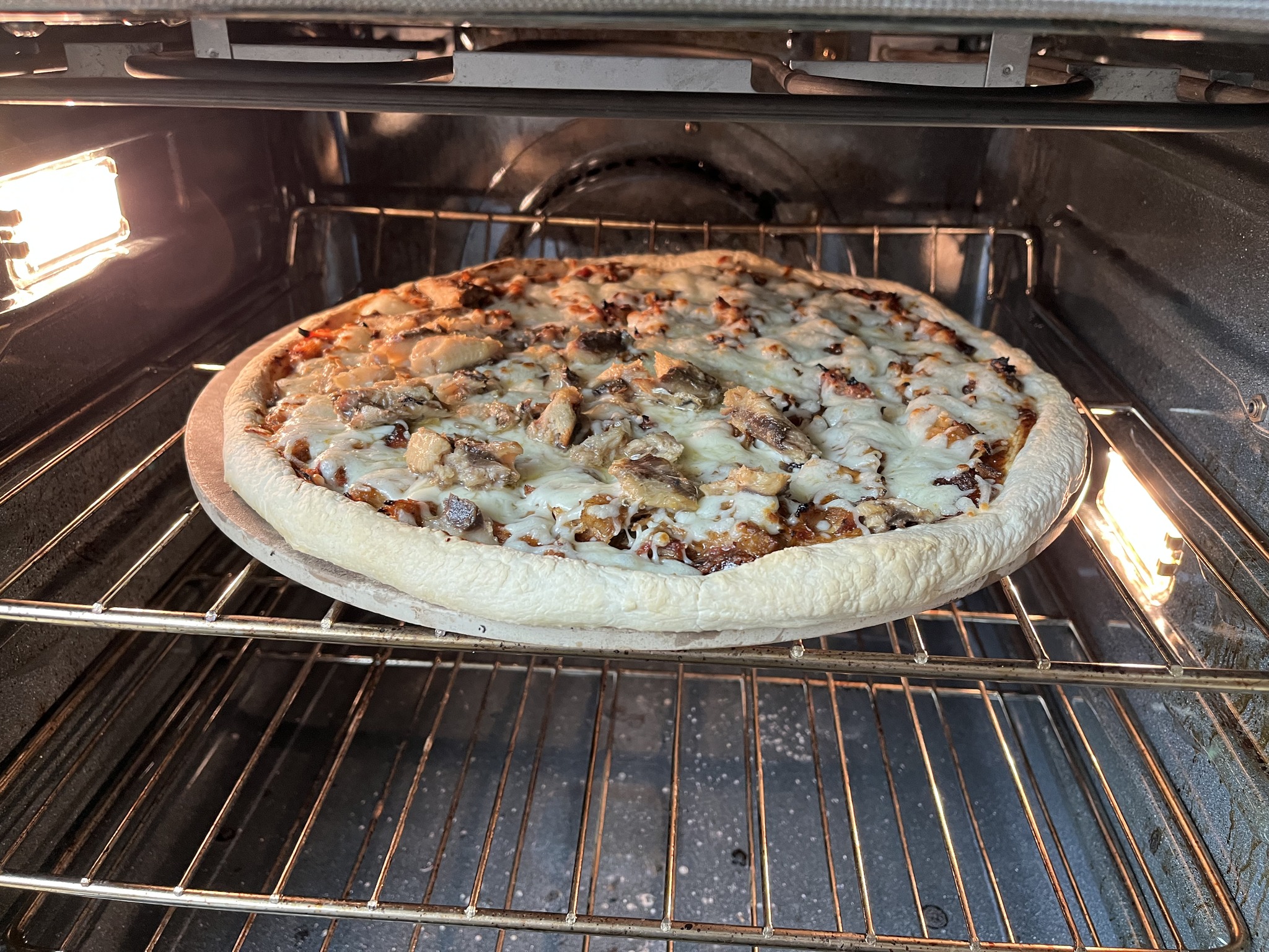 A cheese-and-mushroom pizza baking on a round stone inside the kitchen oven.