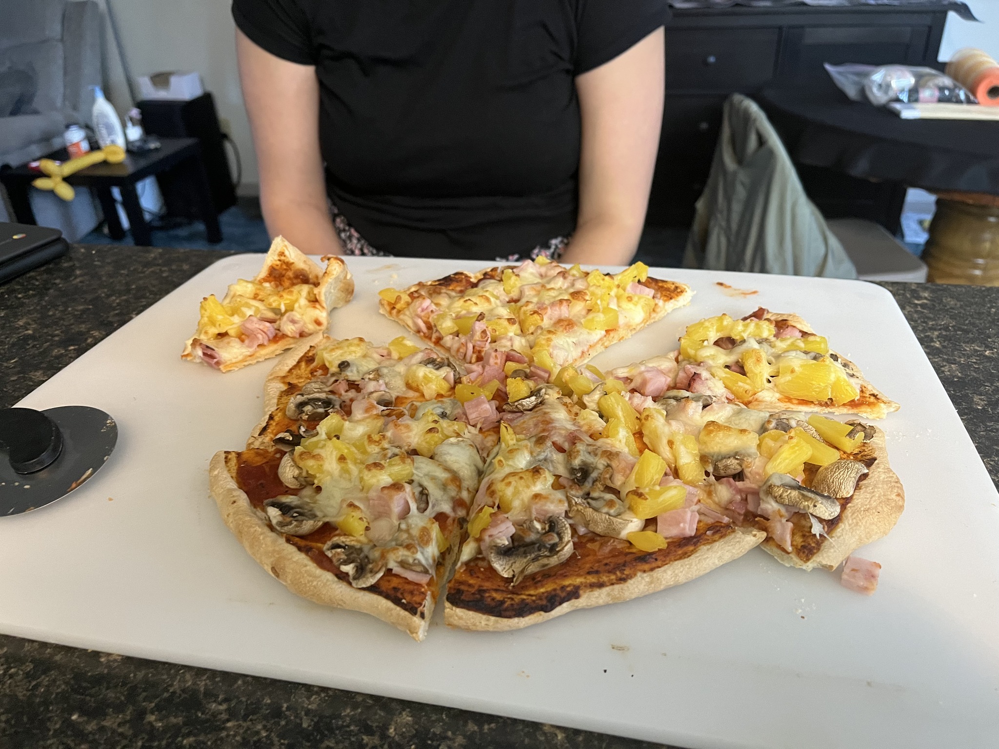 A sliced pizza with mushrooms and pink and yellow toppings on a white cutting board.