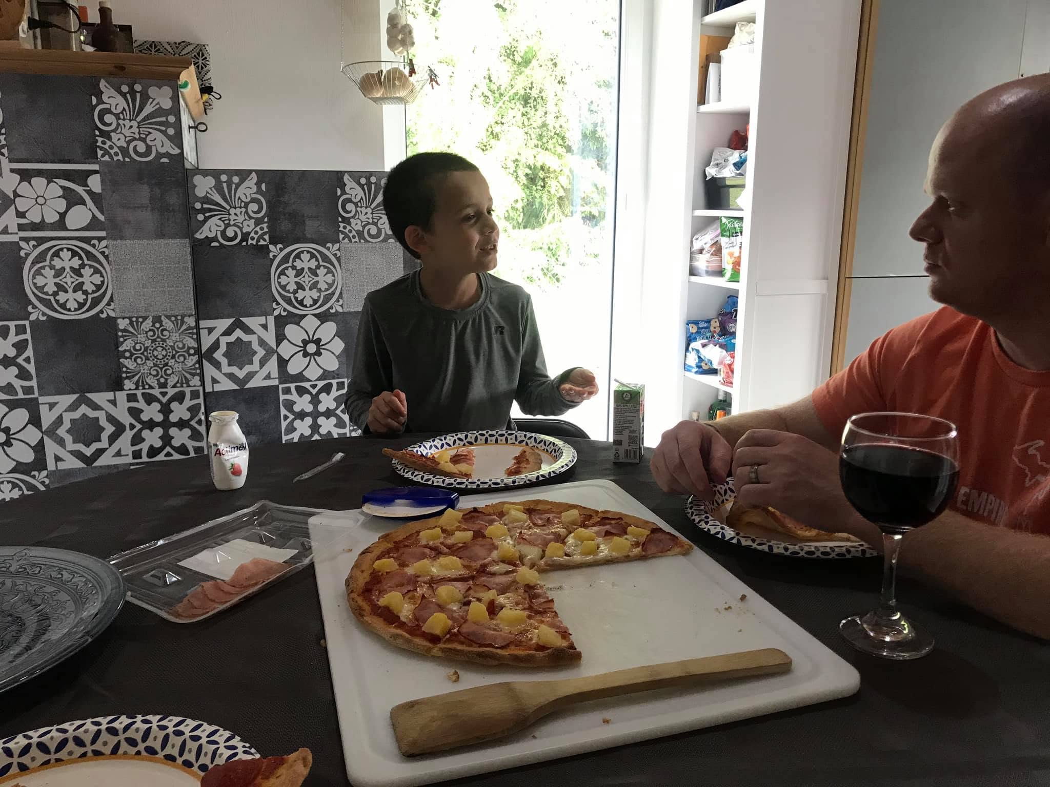 Family eating pizza at the table, with the partially sliced pineapple pizza on a cutting board.