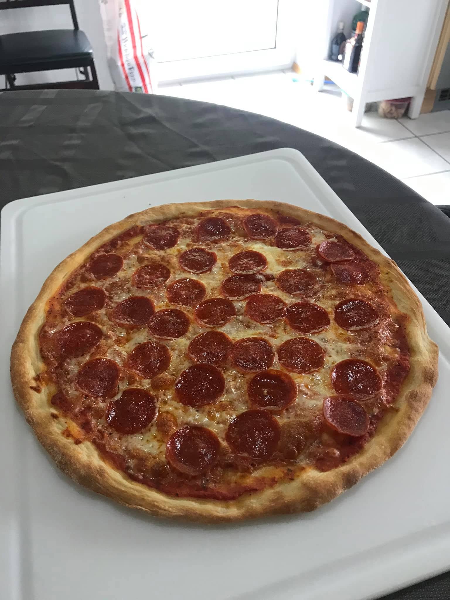Pepperoni pizza with melted cheese and a browned raised rim on a white cutting board.