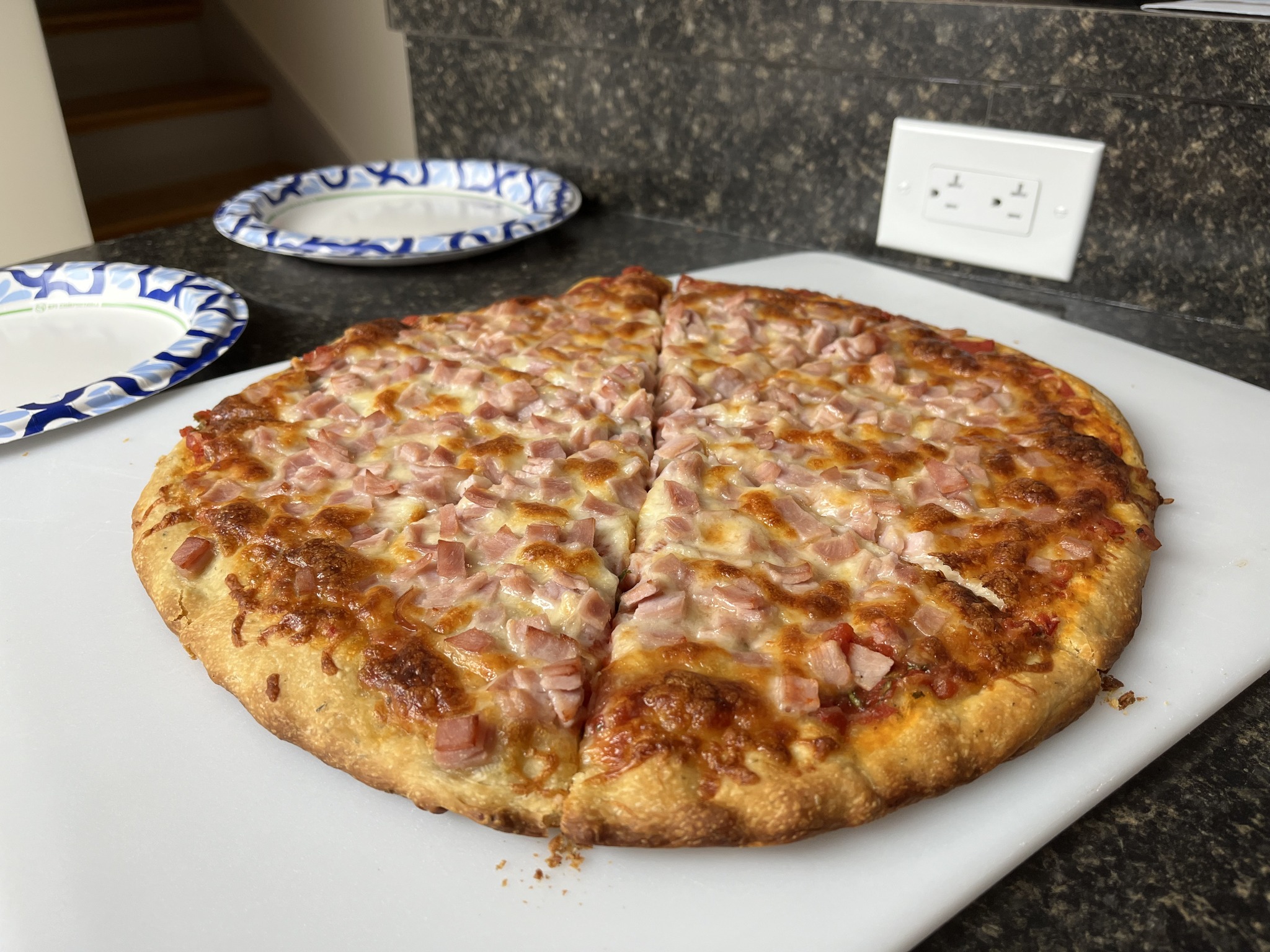 A sliced pizza covered with browned cheese and pink diced topping on a white board.