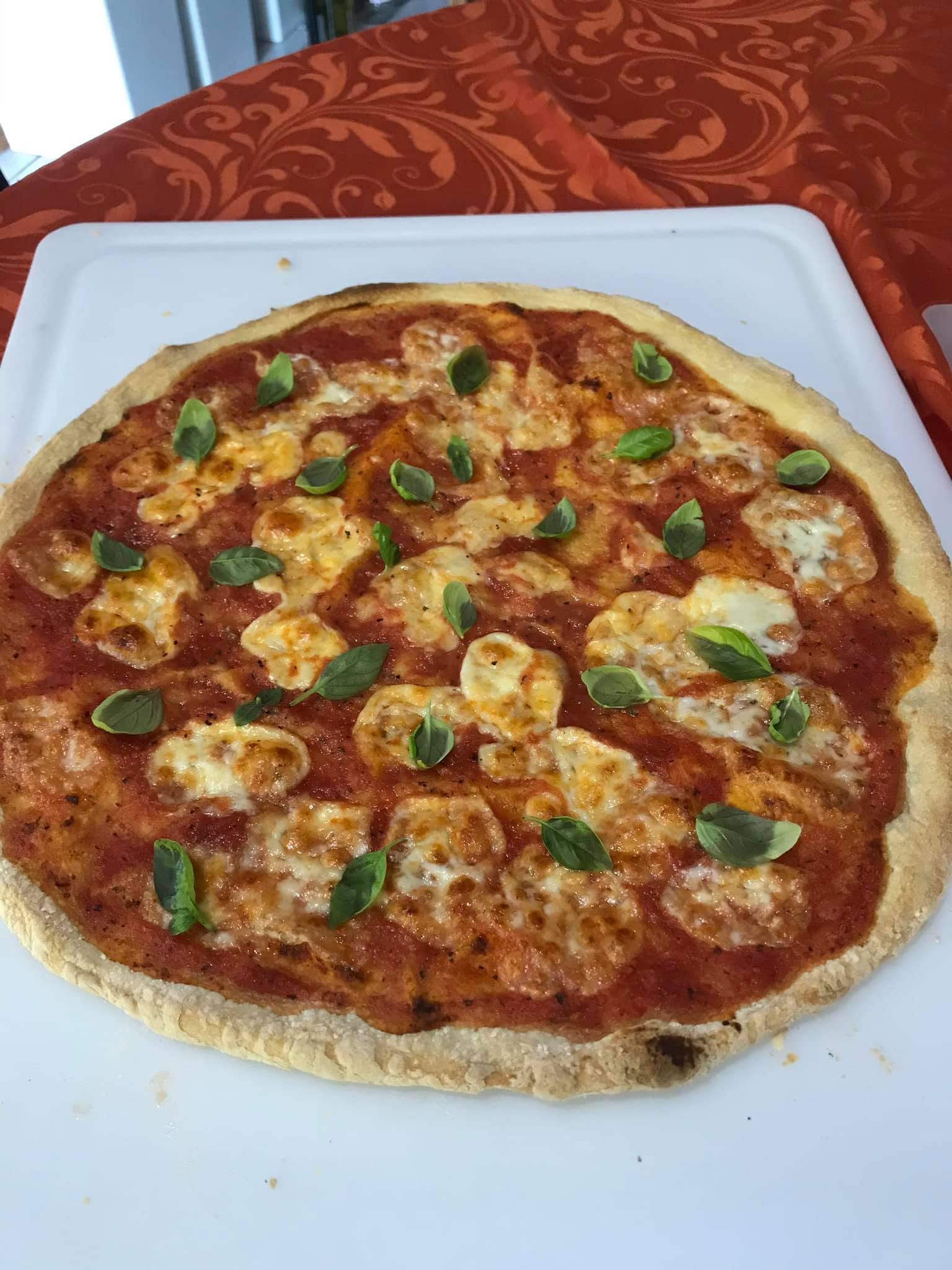 A red-sauced pizza with browned islands of white cheese and small green leaves that appear to be basil.