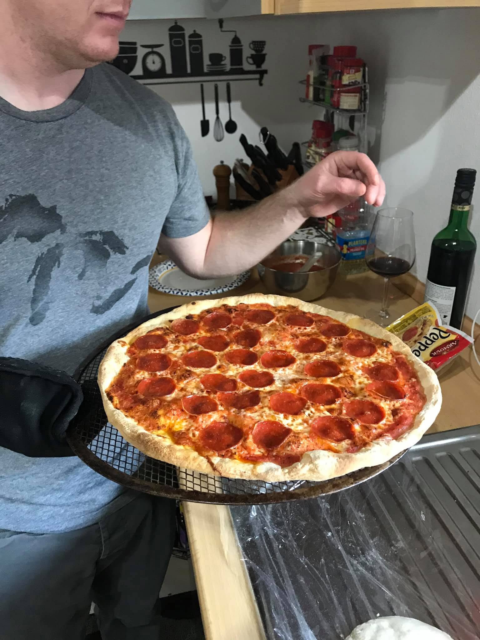 Homemade pepperoni pizza held on a mesh pizza screen beside the kitchen counter.