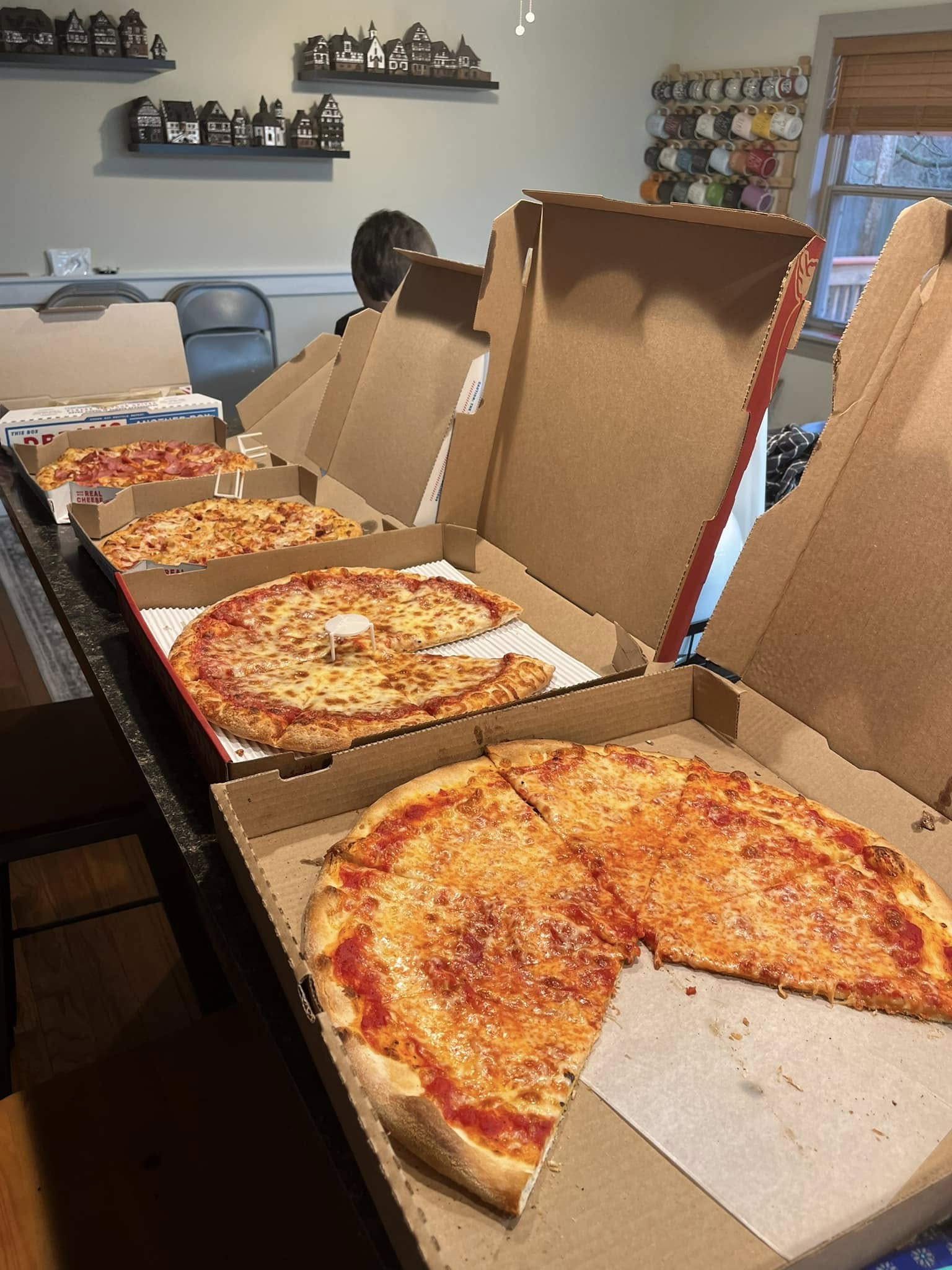Several pizzas in open boxes lined up for the taste test, with slices removed.