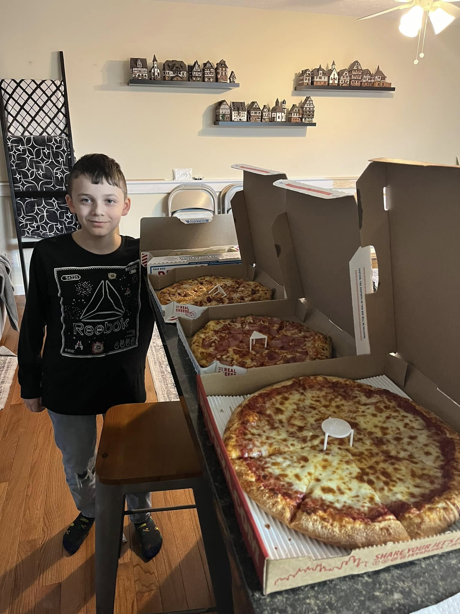 A child beside several open pizza boxes lined up on a counter.