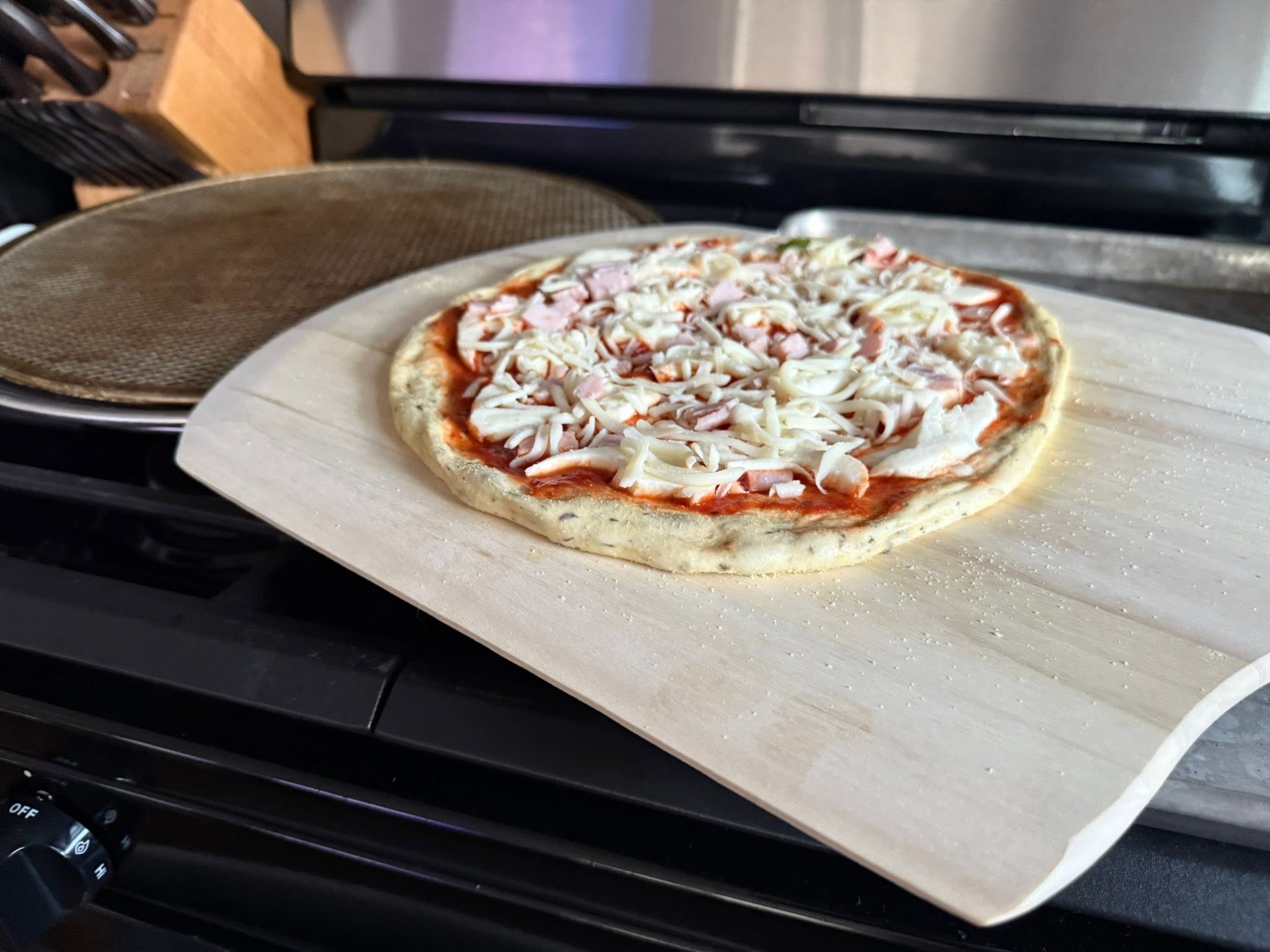 An uncooked pizza topped with sauce, cheese and diced pink meat on a wooden pizza peel.