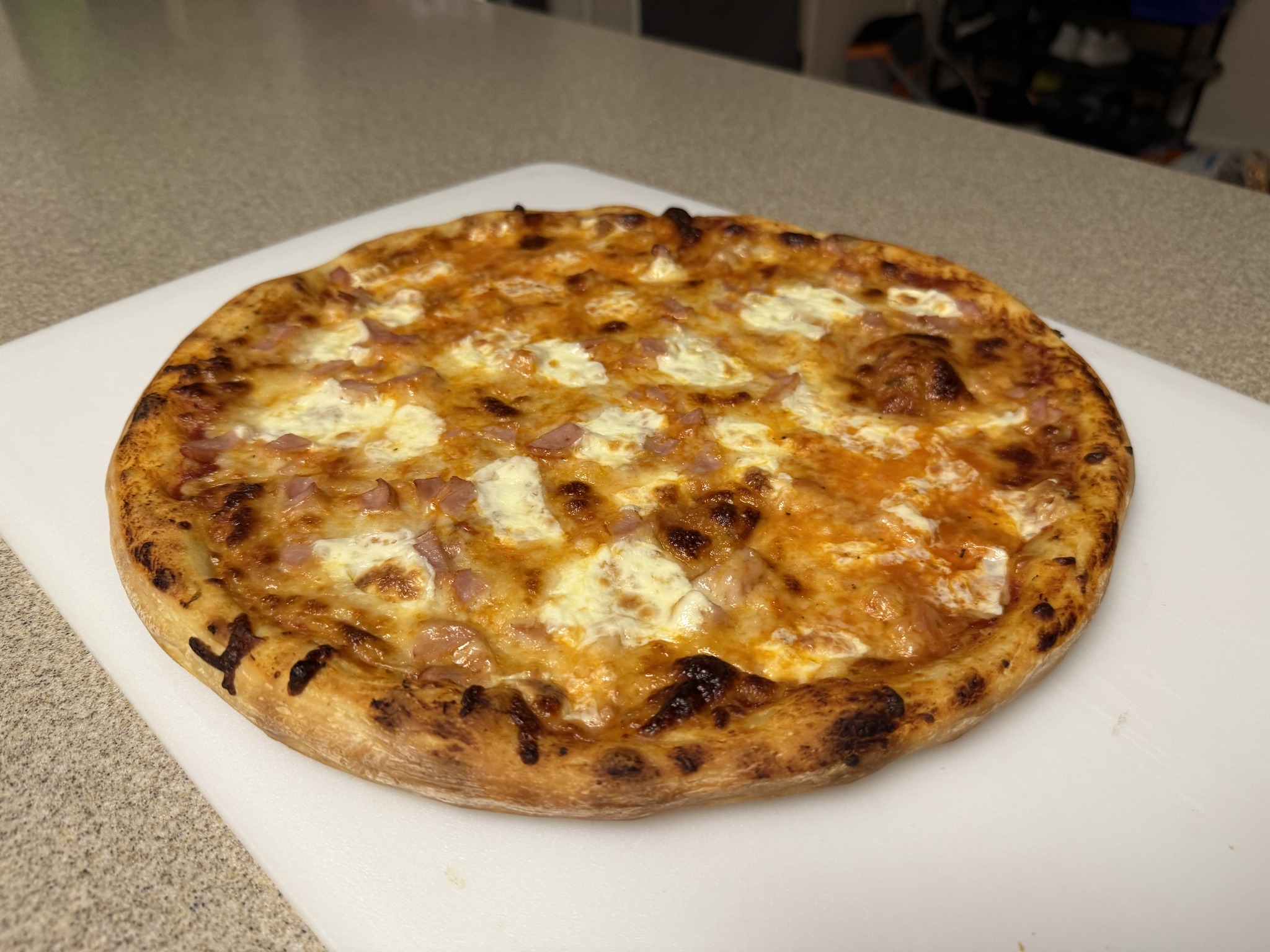 A round pizza with golden cheese, white cheese dollops and small pink topping pieces on a cutting board.