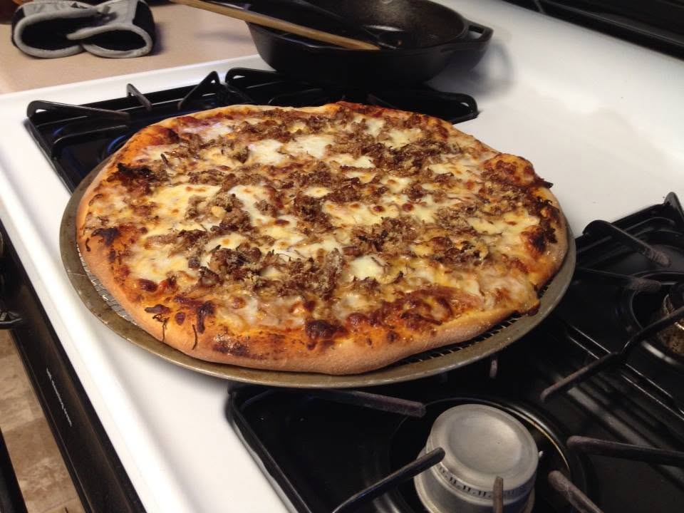 Pulled-pork pizza with melted cheese on a round pizza screen over the stove.