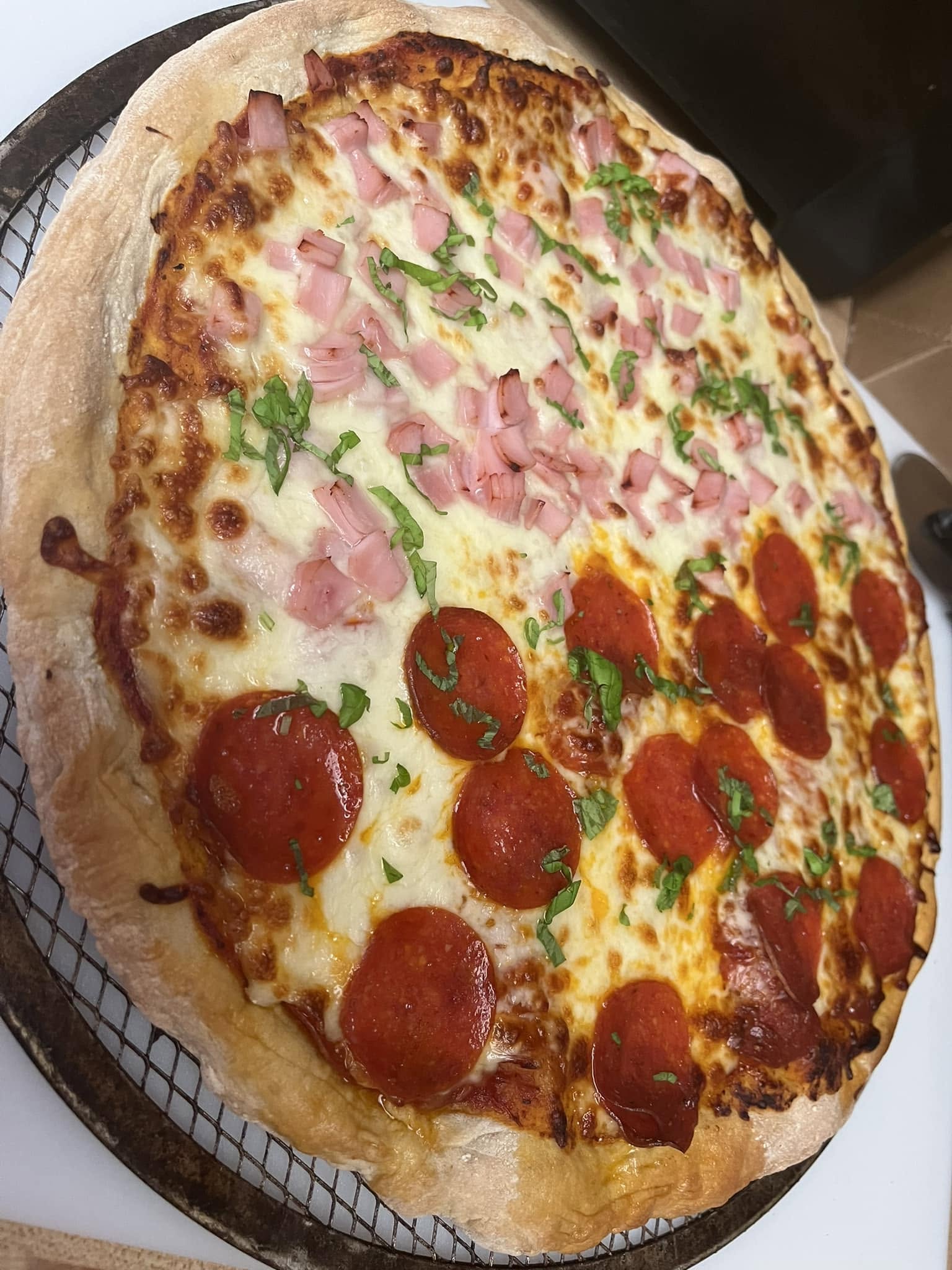 A baked pizza on a round screen, with pepperoni on one half and diced pink toppings on the other.