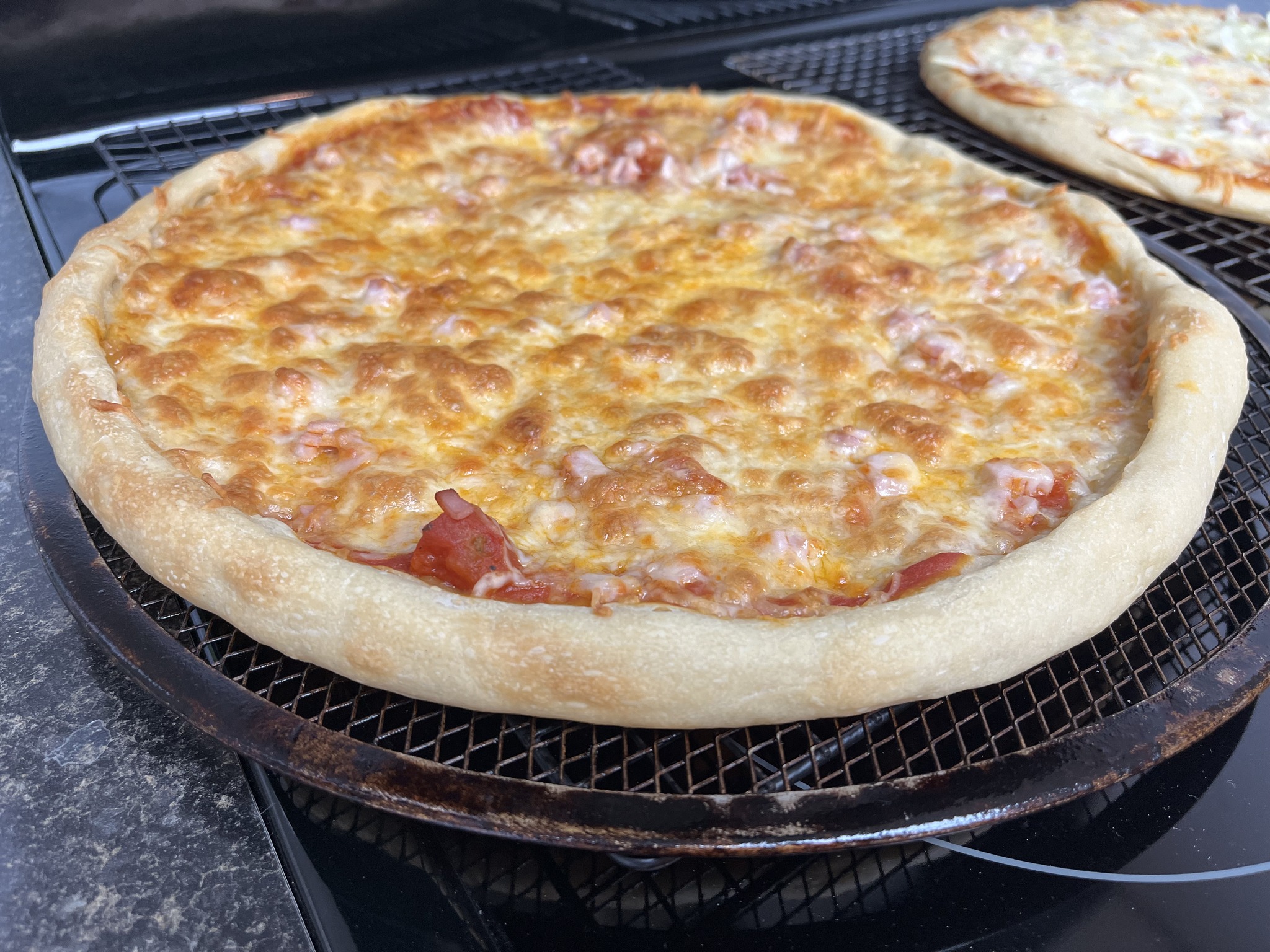 A cheese pizza with a pink diced topping and a pale raised rim on a round pizza screen.