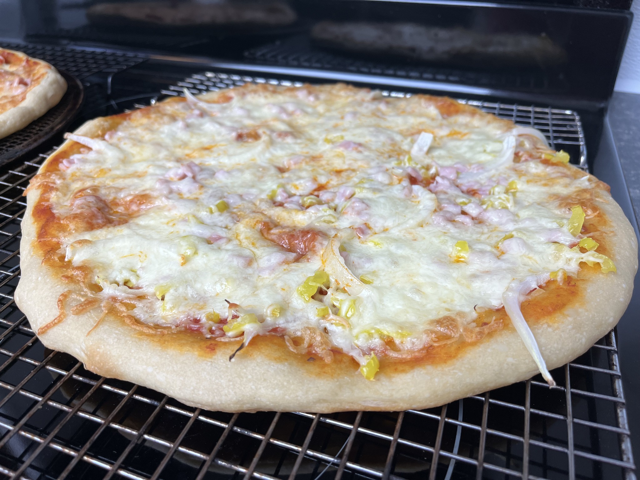 A finished pizza with sliced onion, pink diced topping and yellow-green pepper-like pieces on a cooling rack.